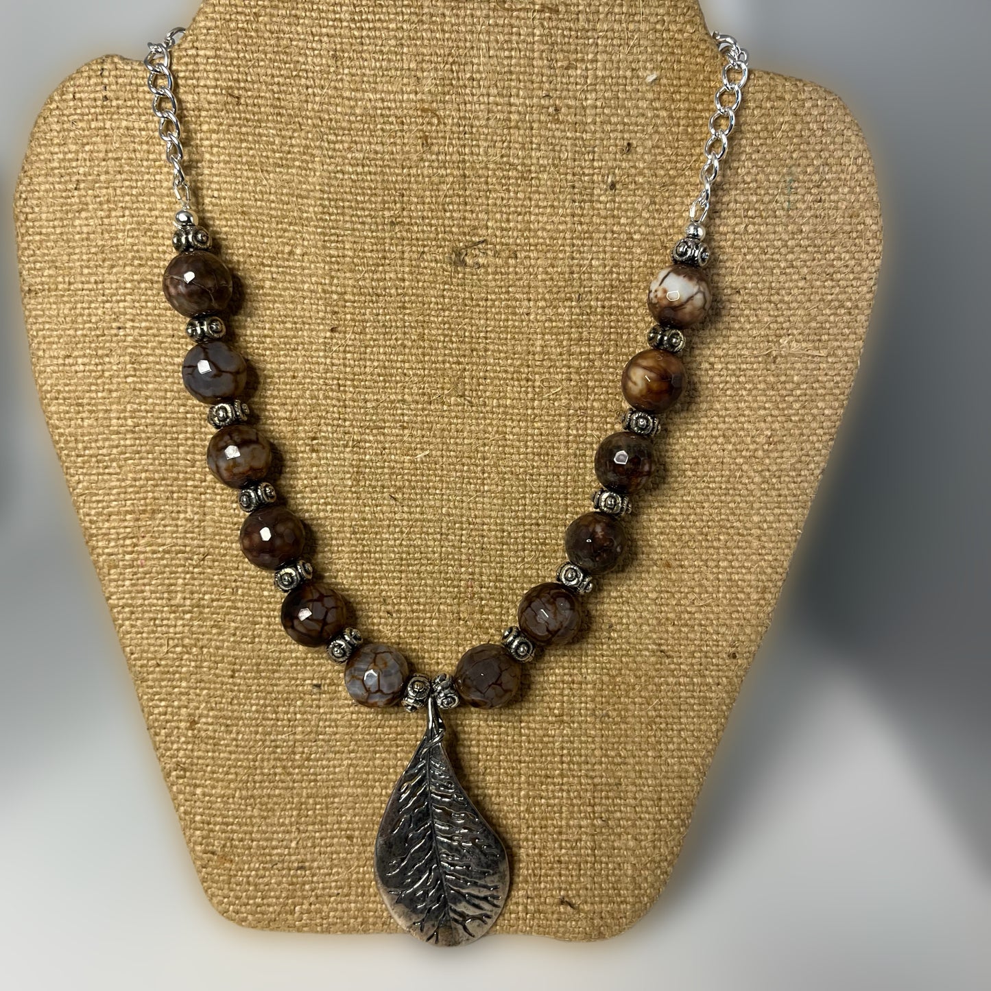 This is a 20 inch necklace made with 12 mm beads attached to silver tone chain. The focal is a large antique silver leaf.