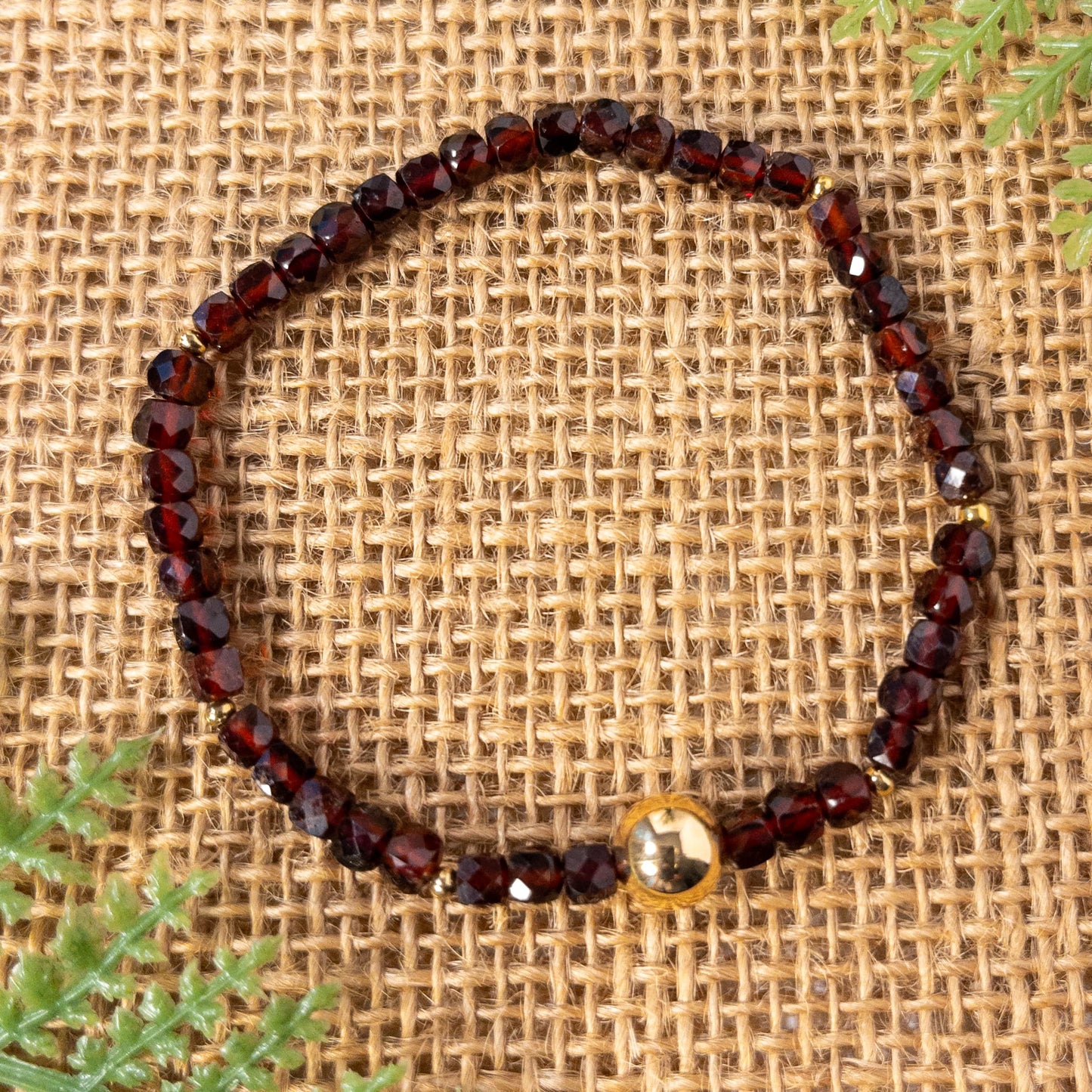 This is a stretch bracelet made with cube shaped faceted garnet beads. It include round gold spacer beads and an 8mm gold plated focal bead.