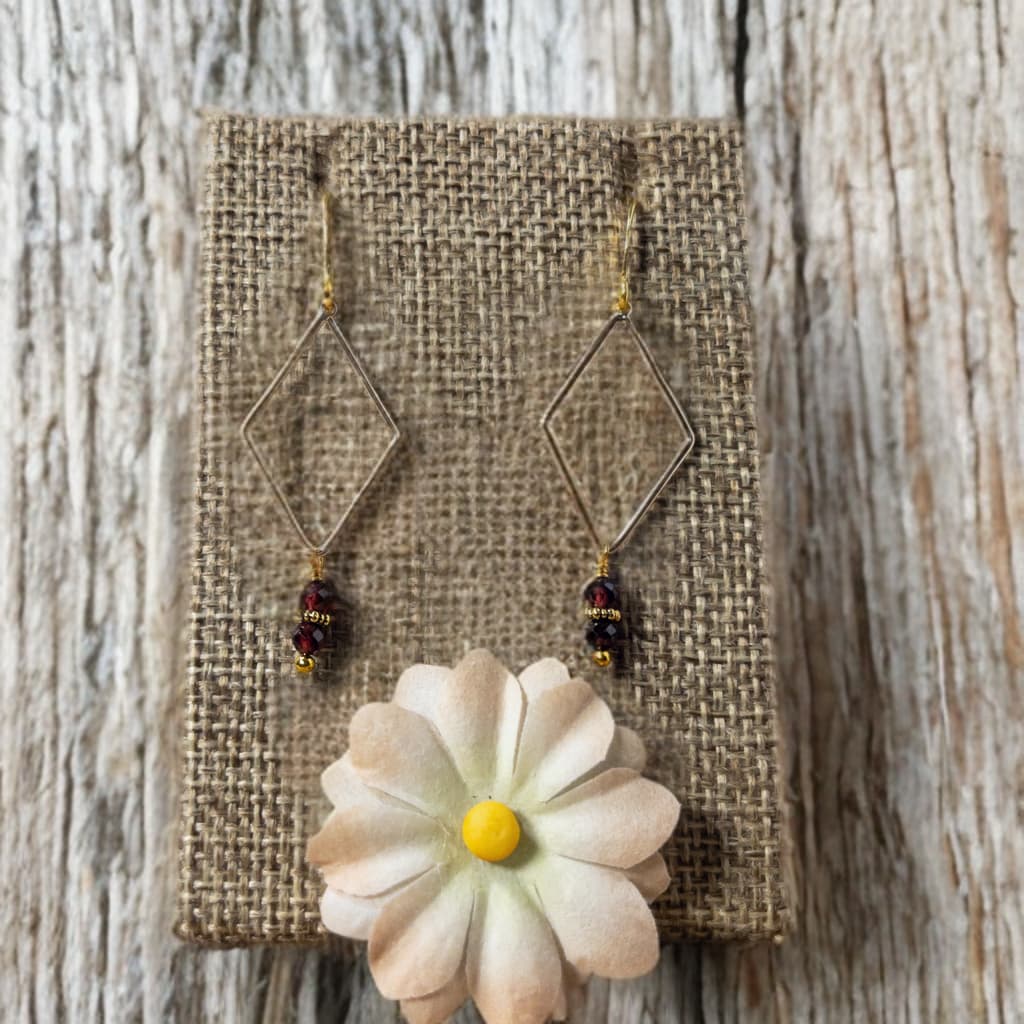 Earrings feature a gold plated rhombus component. 3 mm faceted garnet beads hang from the component. Approximately 2 inches in length
