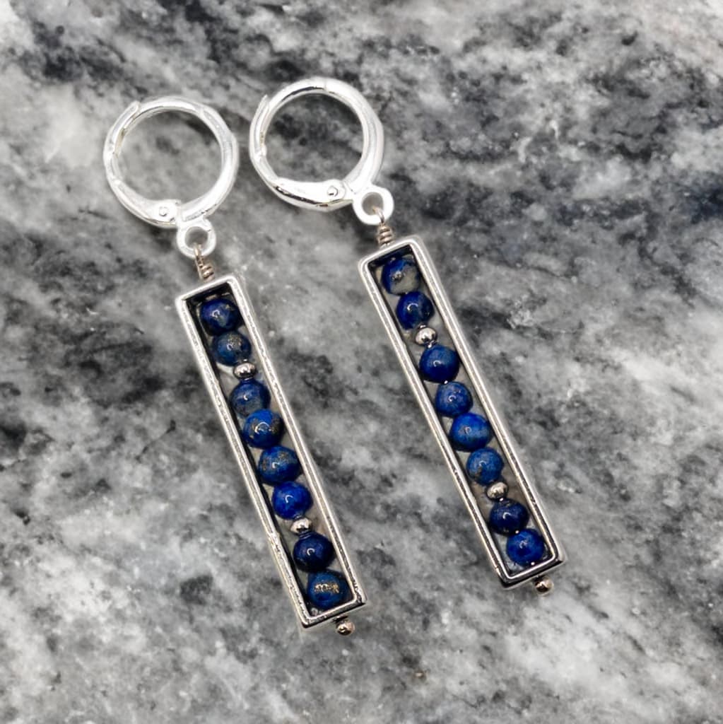 Round 3mm lapis beads are enclosed in a silver tone rectangle bead frame and are suspended from sterling silver huggie ear wires