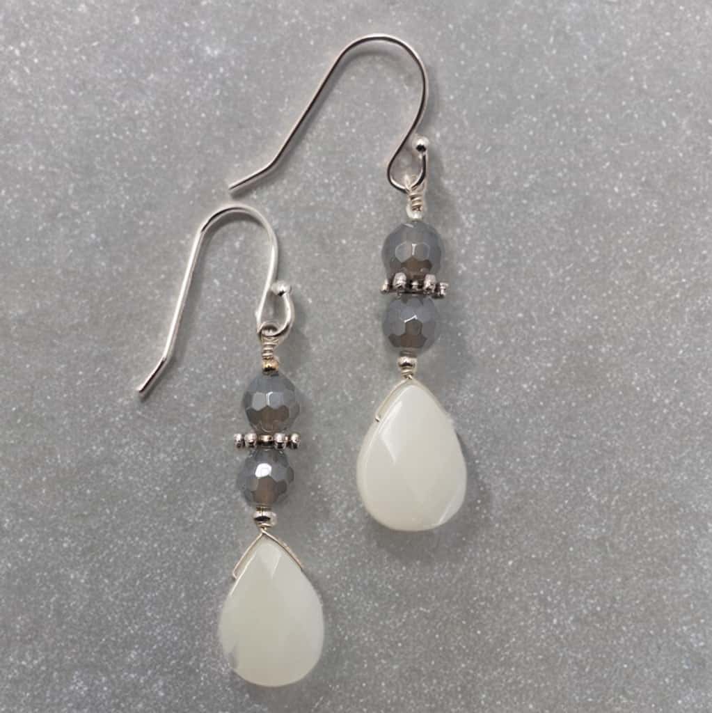 These earrings have an approximate 1.5 inch drop and include faceted grey quartz beads separated by silver tone daisy spacer beads and accented with a tear drop mother of pearl bead.