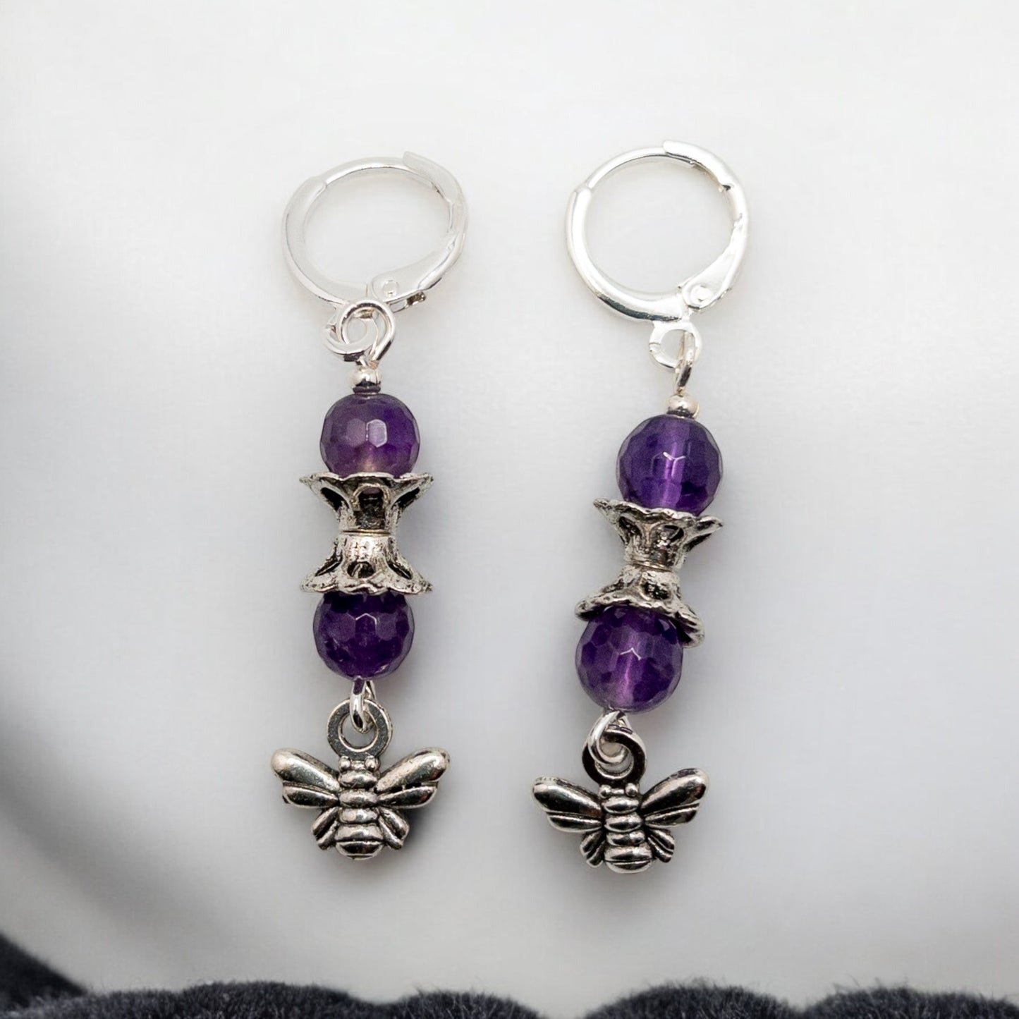 Earrings are made from 6mm faceted amethyst beads that are strung from sterling silver huggie ear wires and accented with a silver tone bee charm