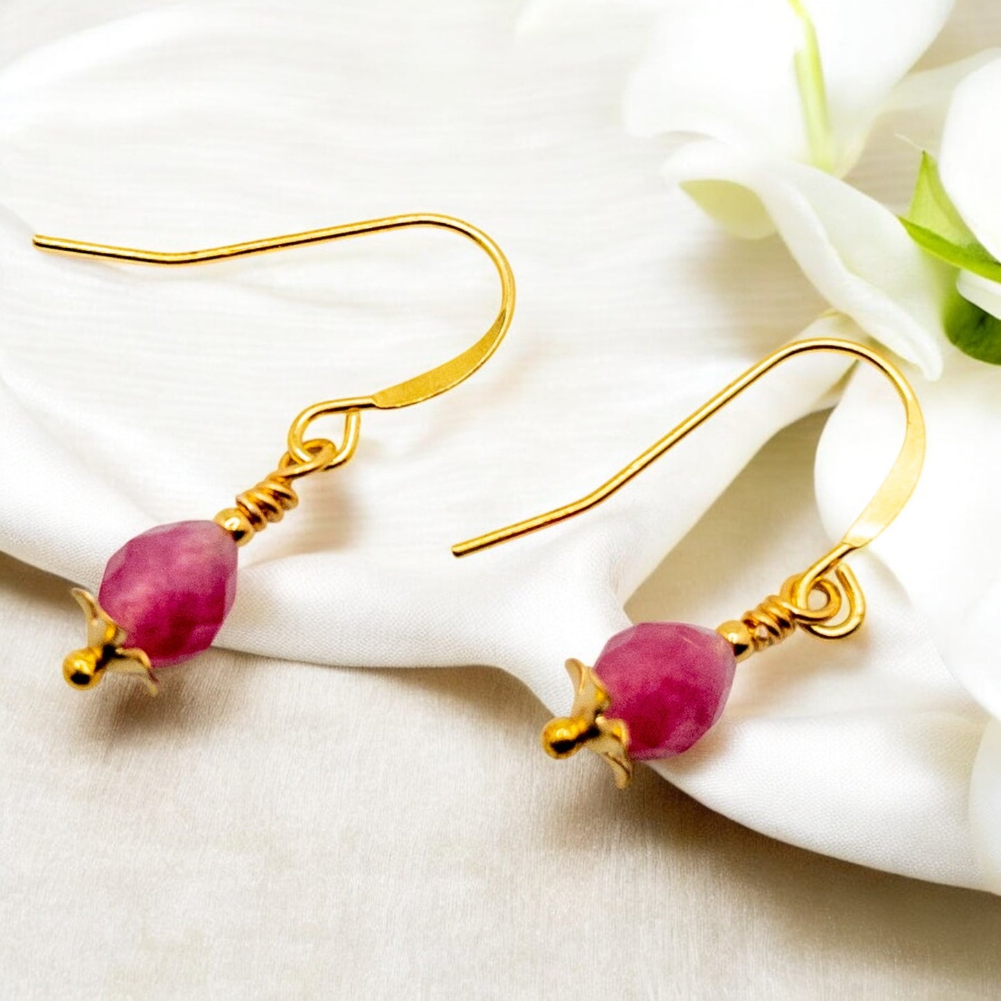 Gold earrings with pink jade beads on a white fabric background