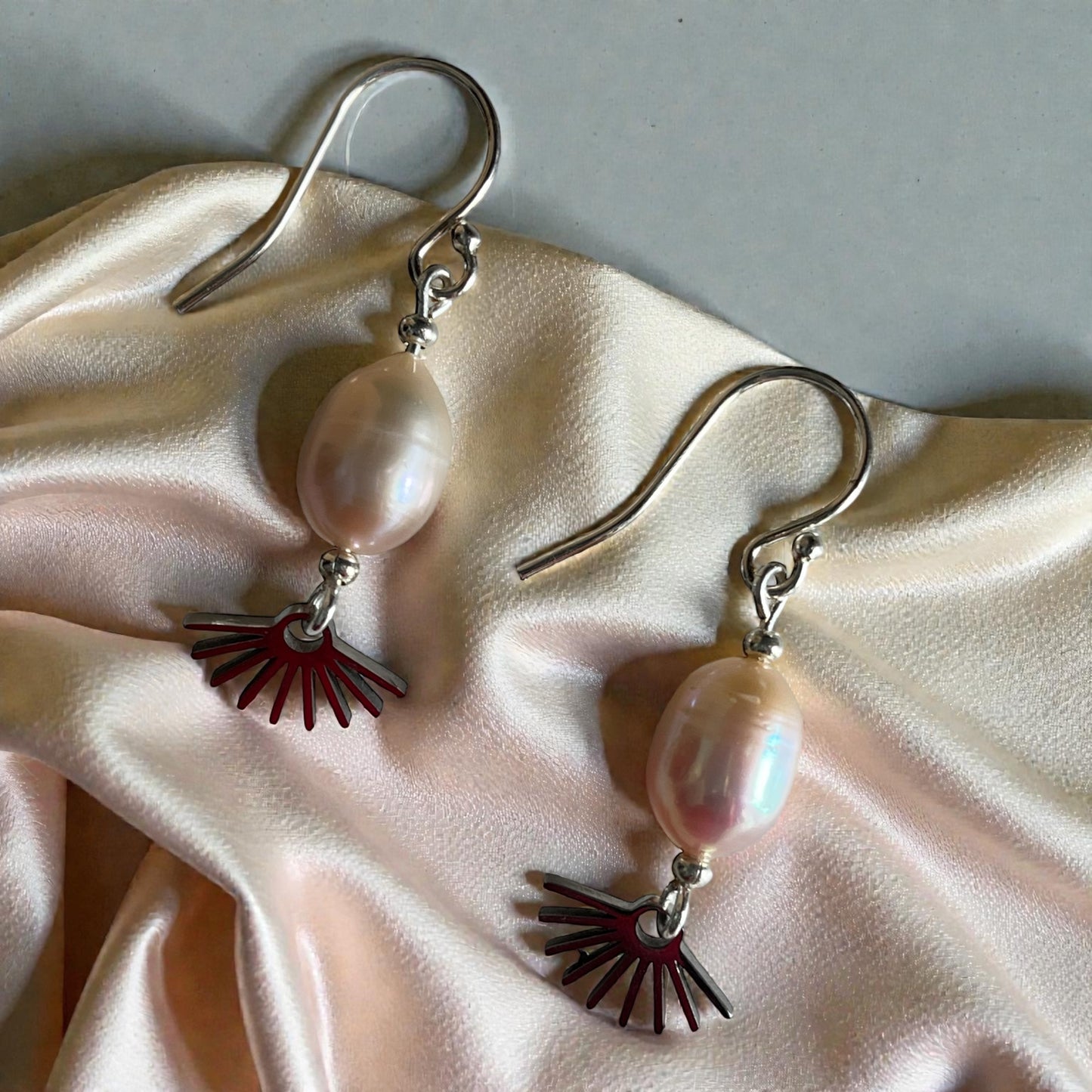 Pair of earrings with pink pearls and sunburst charms on a beige fabric background