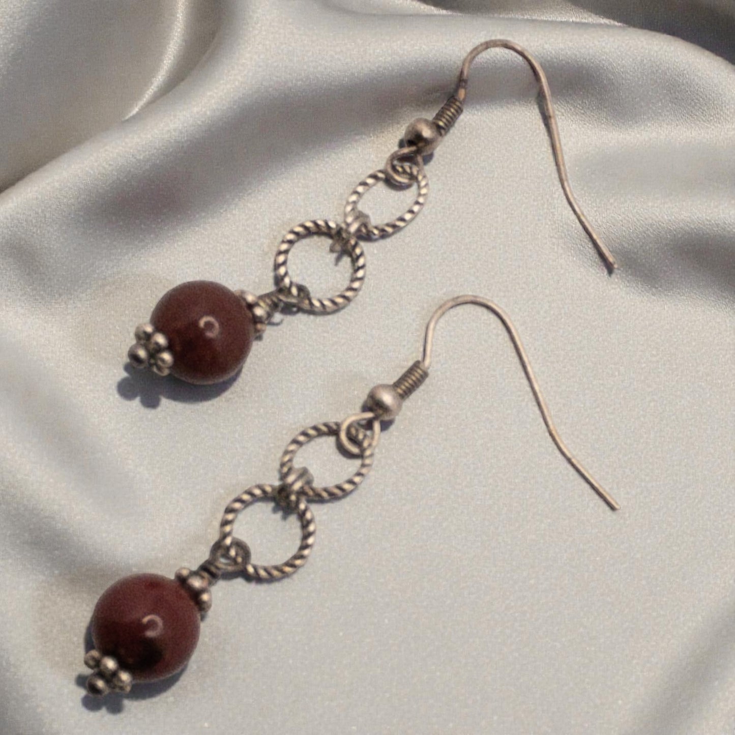 Pair of earrings with brick red bead and silver loops on a light fabric background
