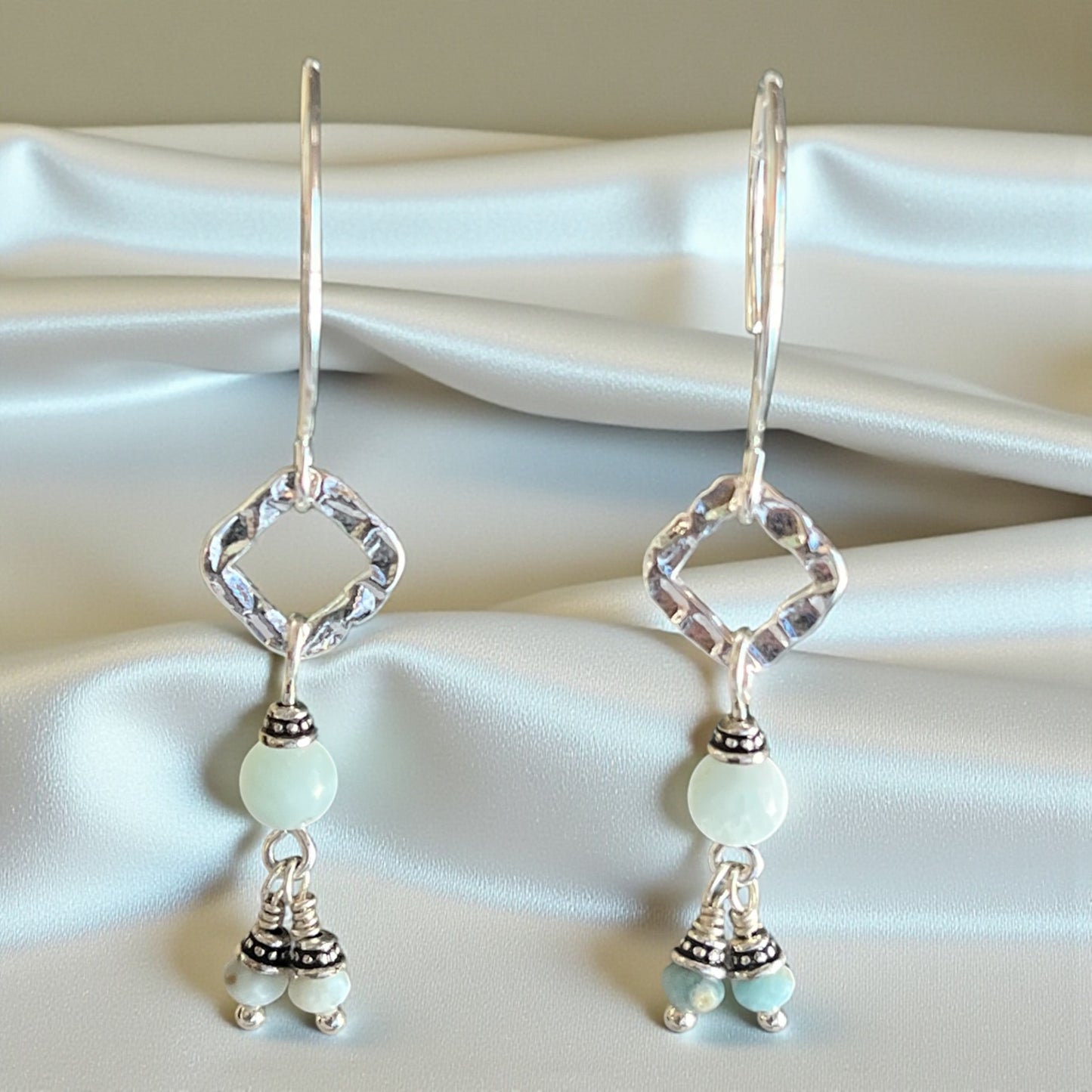 Pair of silver earrings with light green beads on a white fabric background