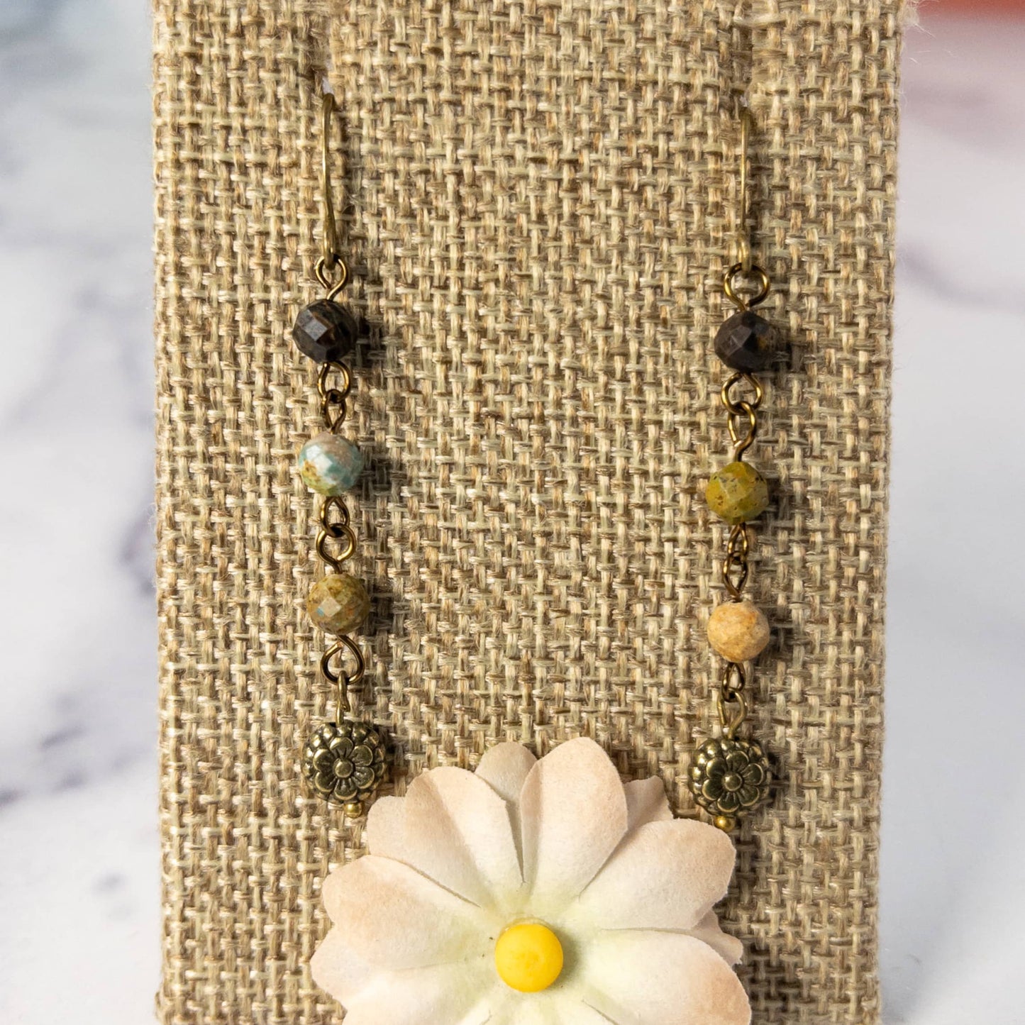 Measuring 1.5 inches in length, these earrings feature a beaded chain made from small faceted turquoise beads and are finished with an antique bronze flower charm.