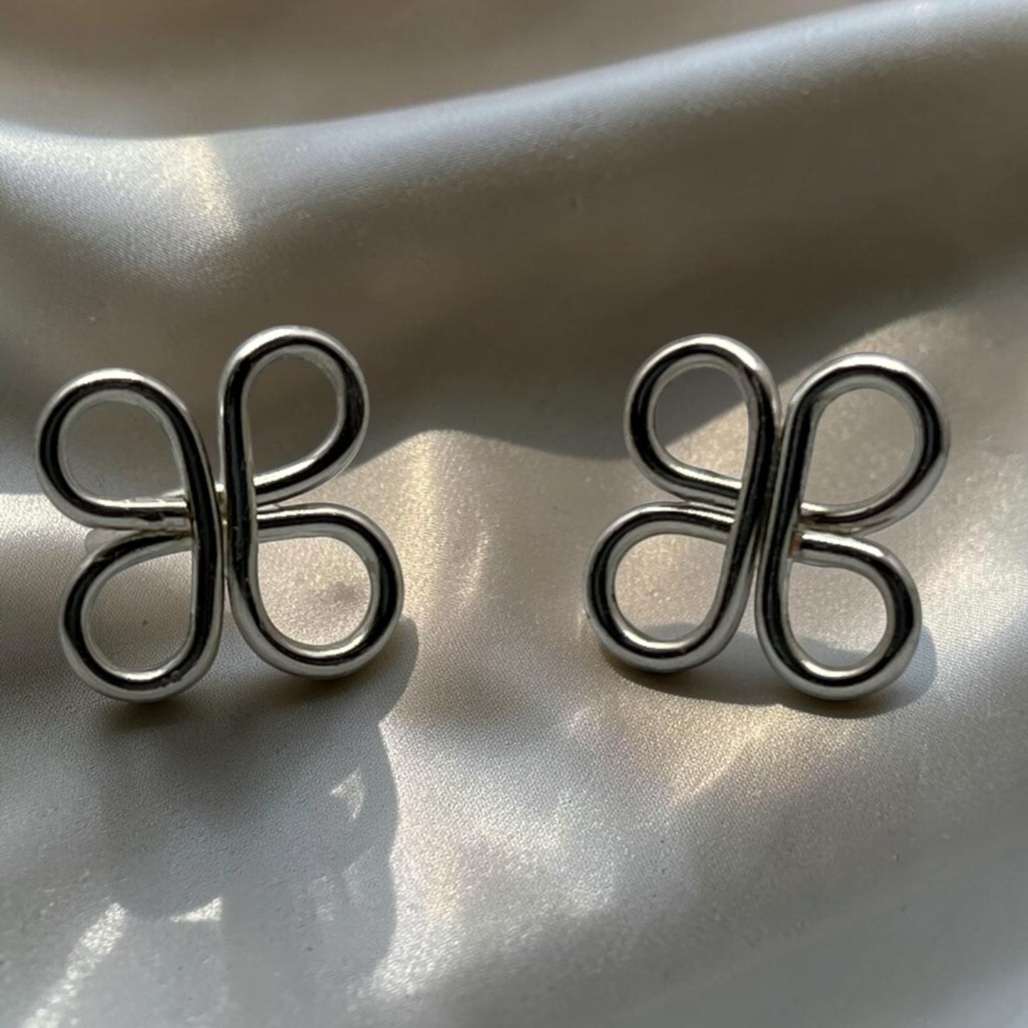 Blakeley Lane Jewelry silver-toned sculptural loop stud earrings with a polished clover-inspired open-work design.