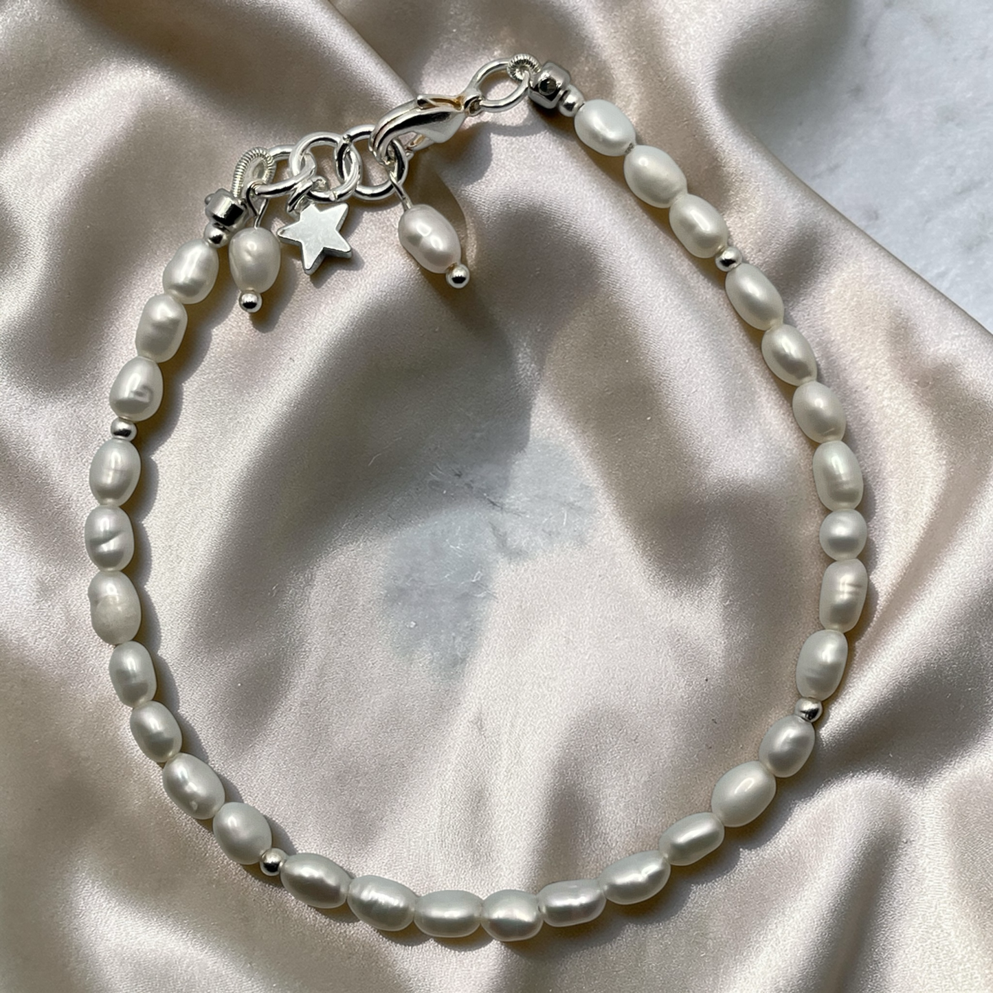 Pearl bracelet with silver charms on a satin surface