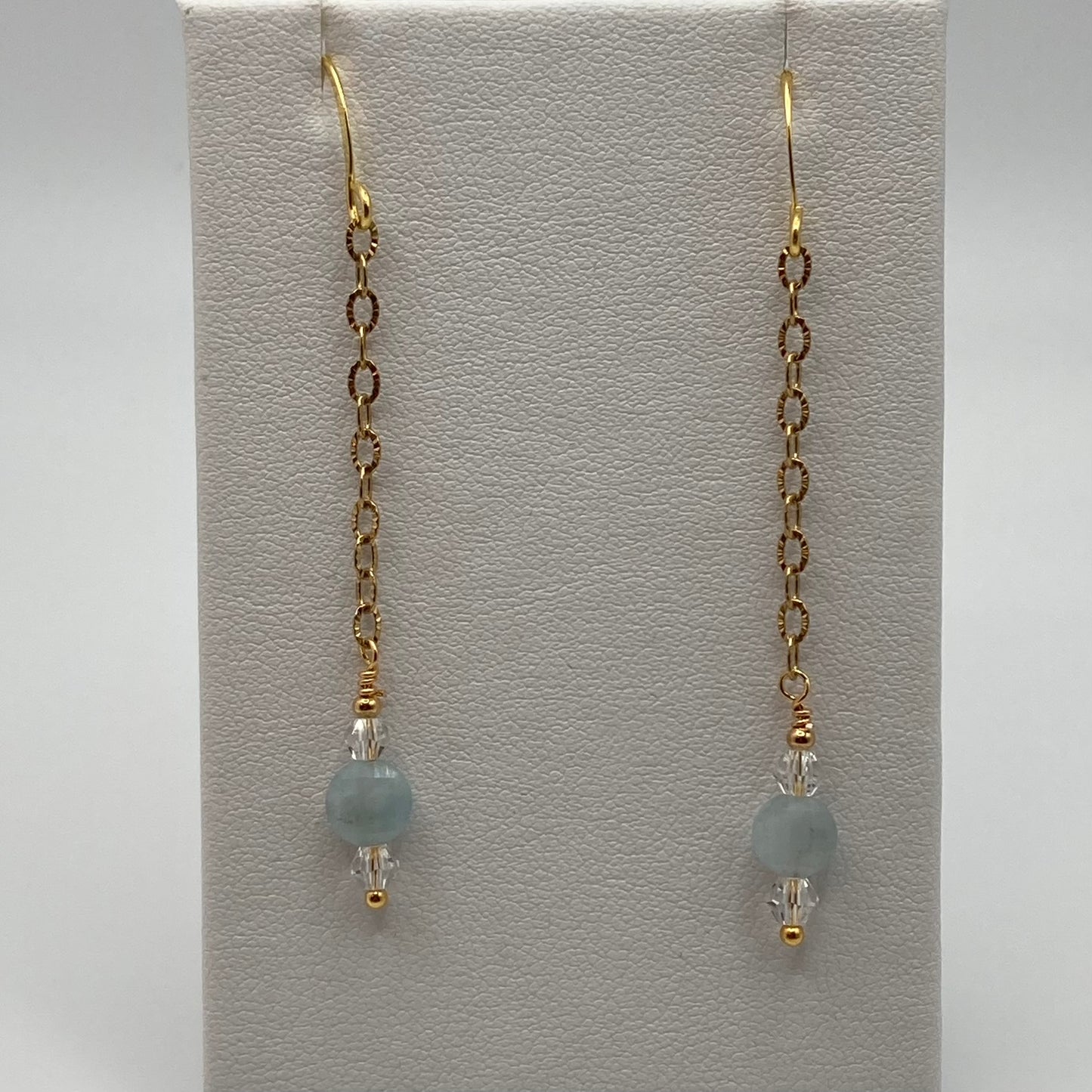 Checkerboard coin-shaped Aquamarine beads hang delicately from delicate gold chains. The earring measure approximately 2 inches long