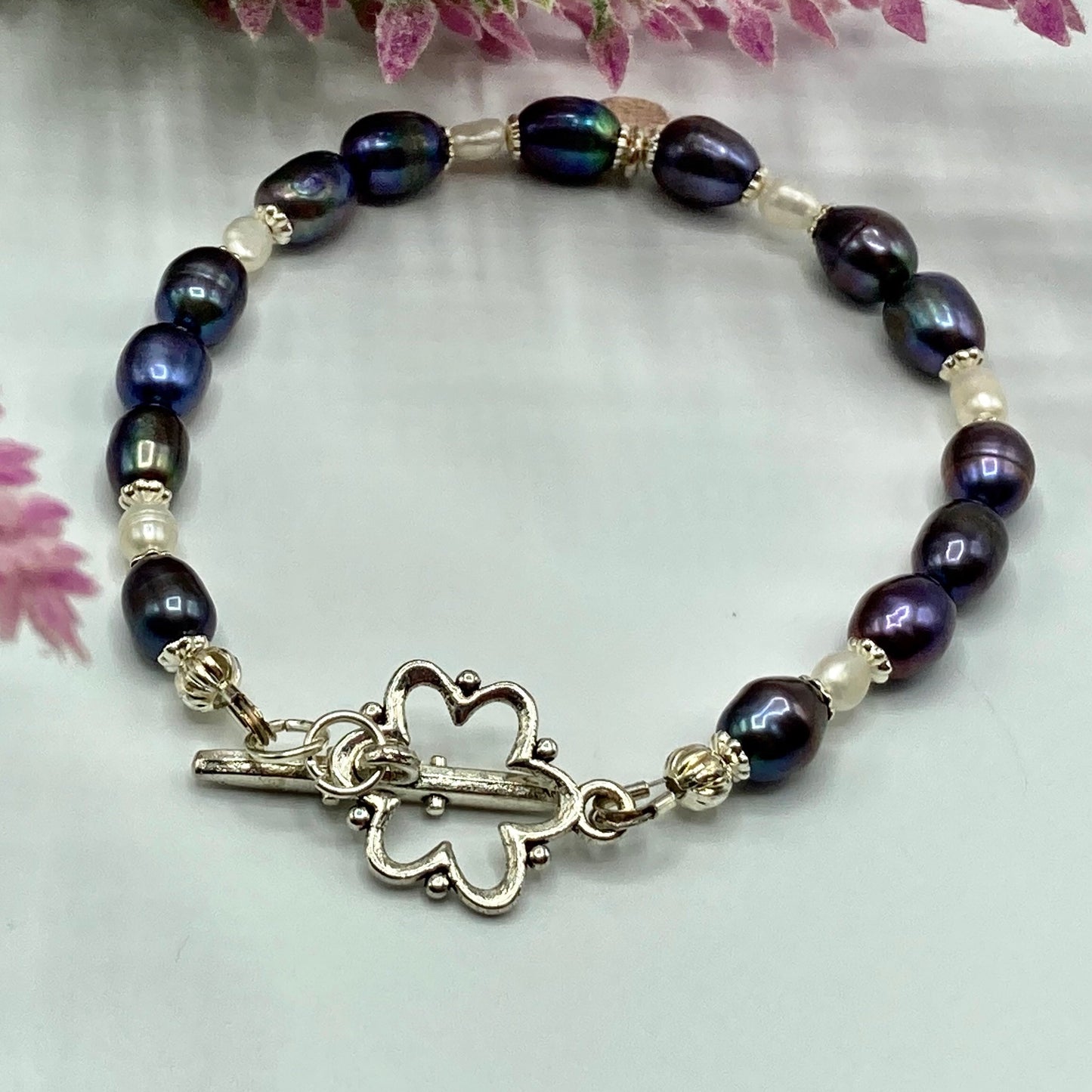 This bracelet is made with freshwater rice pearls in a peacock mix and is ended with a flower-shaped toggle. it fits up to a 7" inch wrist.