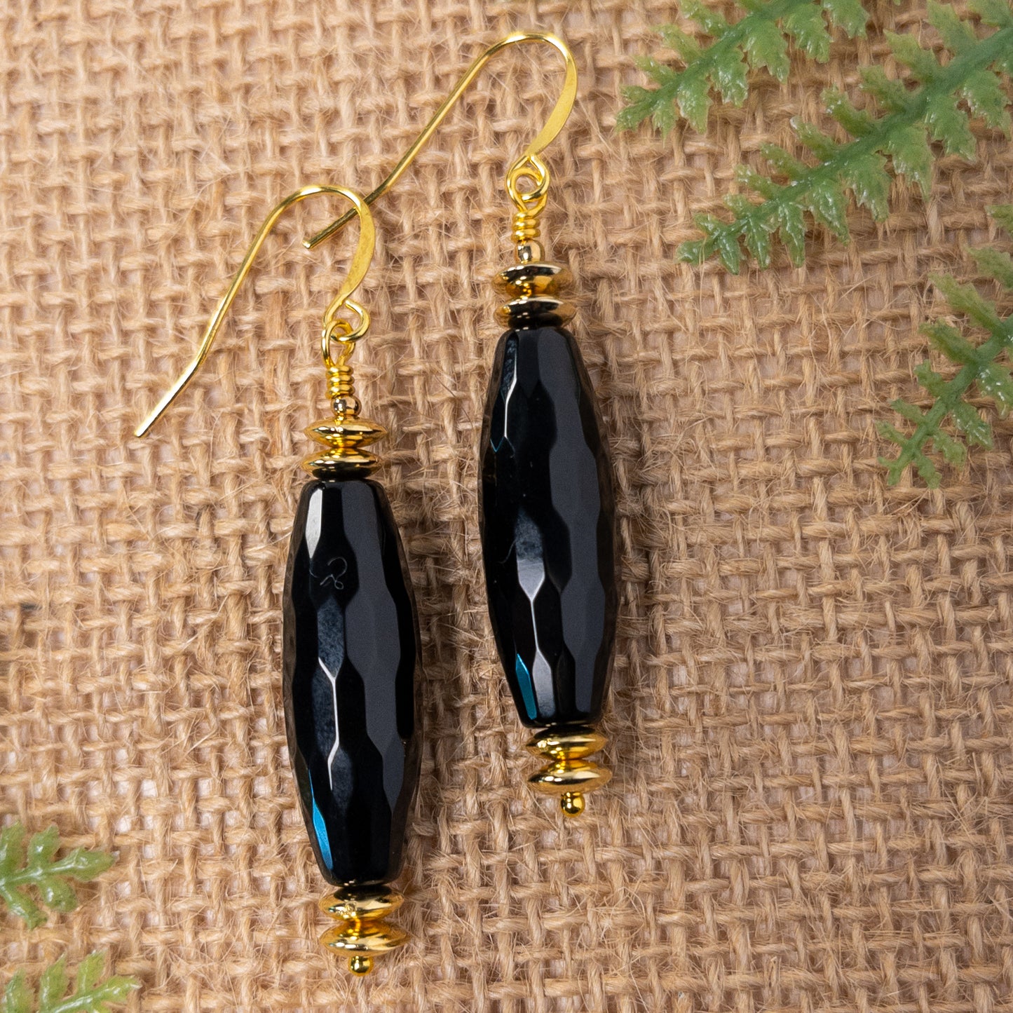 These earrings feature a faceted rice shaped black agate bead that is approximately 1.25 inches in length.  It is accented with gold tone disc shaped spacer beads.
