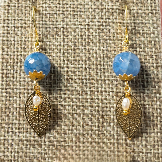 These 1.25 inch earrings feature stunning 10mm Coneflower Fire Agate gemstone beads and elegant filigree leaf charms, creating the perfect balance of delicate and eye-catching. The striking blue tones of the gemstones are beautifully accented by the gold-tone bead caps and leaf charms