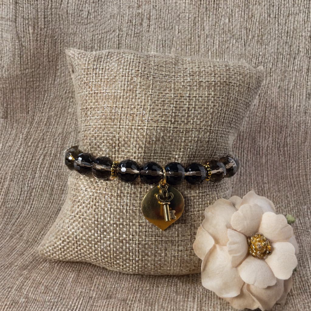 This stretch bracelet is made with faceted smokey quartz beads and accented with gold tone daisy spacer beads.  It include a key charm as its focal.
