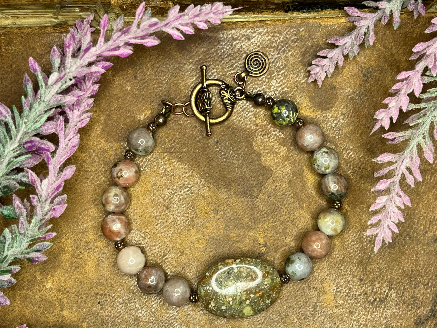 Oval autumn jasper focal bead and round beads accented with copper spacer beads.  The beads include greens, creamy tan, and rose gold .  Toggle clasp