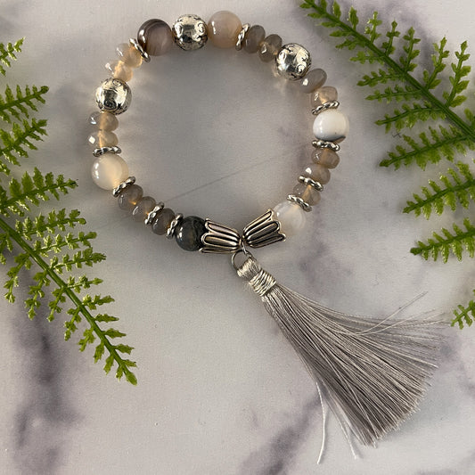 This is a stretch bracelet made with white agate round beads and grey agate rondelles.  Silver tone spacer beads are placed between the beads to provide additional accent.  A soft grey tassel finishes the bracelet