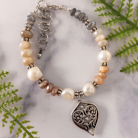 This bracelet is made with moonstone rondelle beads in hues of peach, cream and soft grey.  Potatoe shaped pearls and interspersed in the design.  It includes a heart shaped focal link and a 2 inch extender