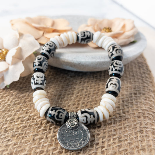 This is a stretch bracelet made with drum-shaped agate beads.  The beads are black with a white design.  Shell puca beads serve as spacers.  The focal of the bracelet is a coin.  
