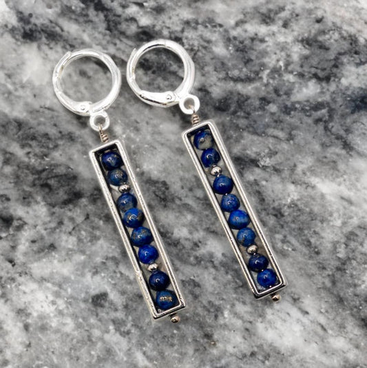 Round 3mm lapis beads are enclosed in a silver tone rectangle bead frame and are suspended from sterling silver huggie ear wires