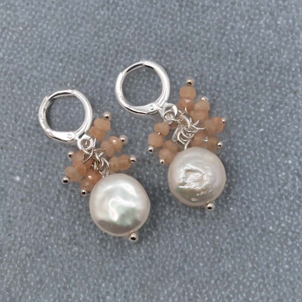 Lustrous freshwater coin pearls are adorned with peach moonstone dangles all hug from sterling silver huggie ear wires.