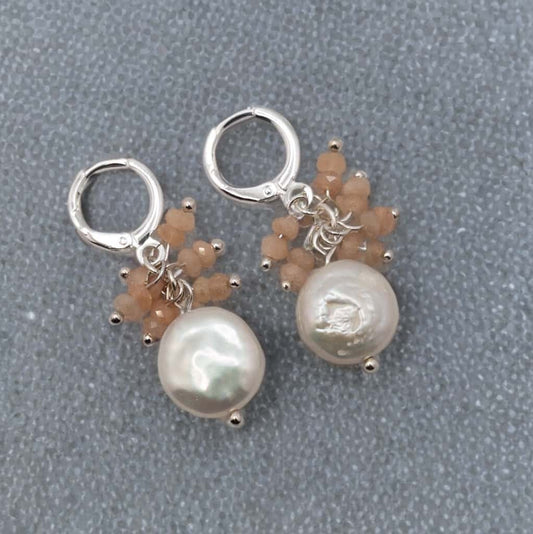 Lustrous freshwater coin pearls are adorned with peach moonstone dangles all hug from sterling silver huggie ear wires.