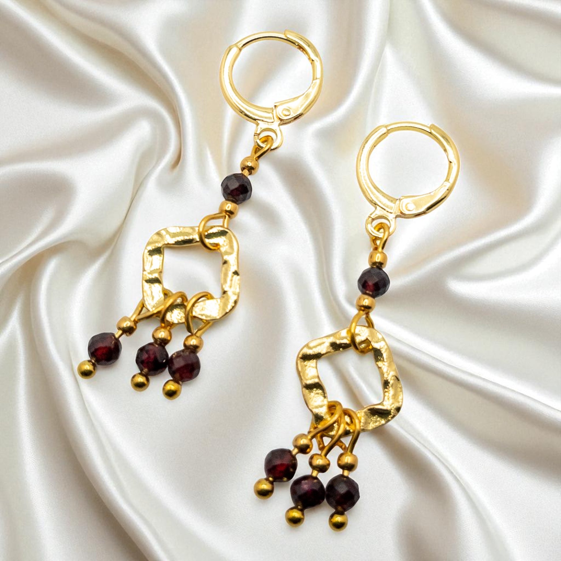 Gold earrings with red gemstones on a satin background
