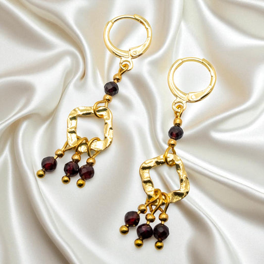 Gold earrings with red gemstones on a satin background