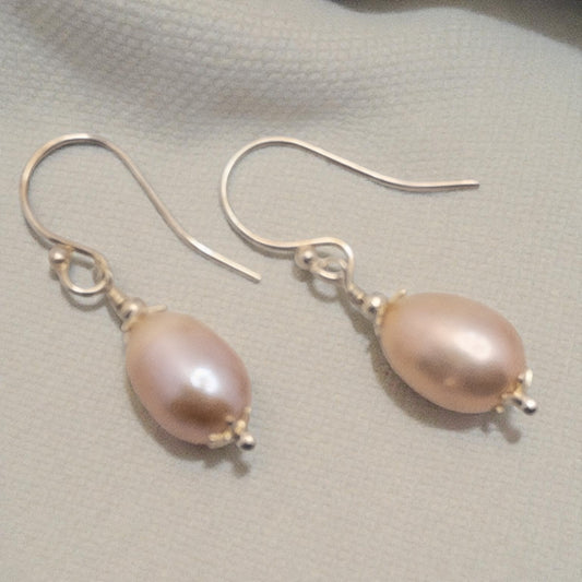 Pair of mauve pearl earrings on a light fabric background