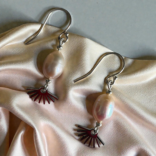 Pair of earrings with pink pearls and sunburst charms on a beige fabric background