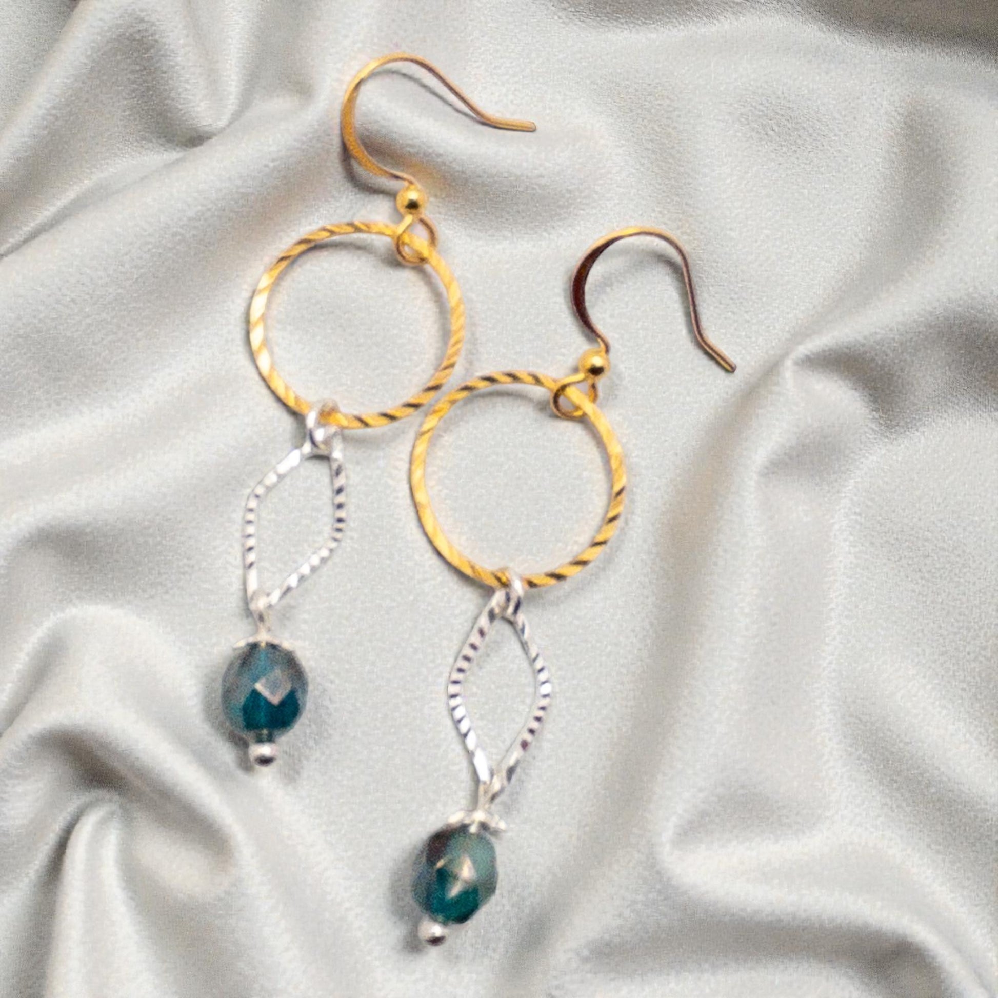 Pair of gold and silver hoop earrings with teal beads on a light fabric background
