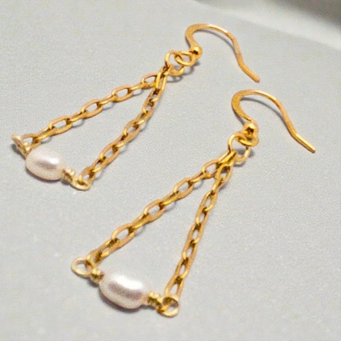 Gold chain earrings with rice pearl  beads on a light gray background