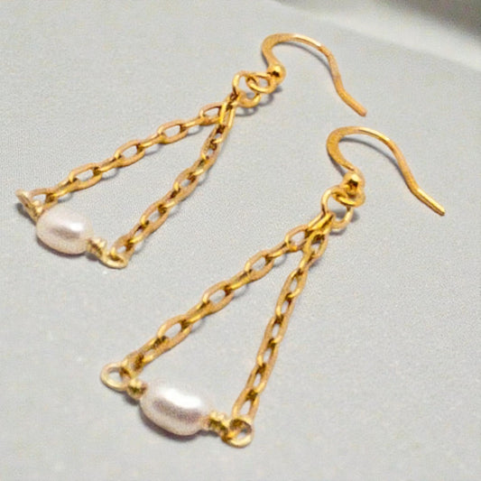 Gold chain earrings with rice pearl  beads on a light gray background