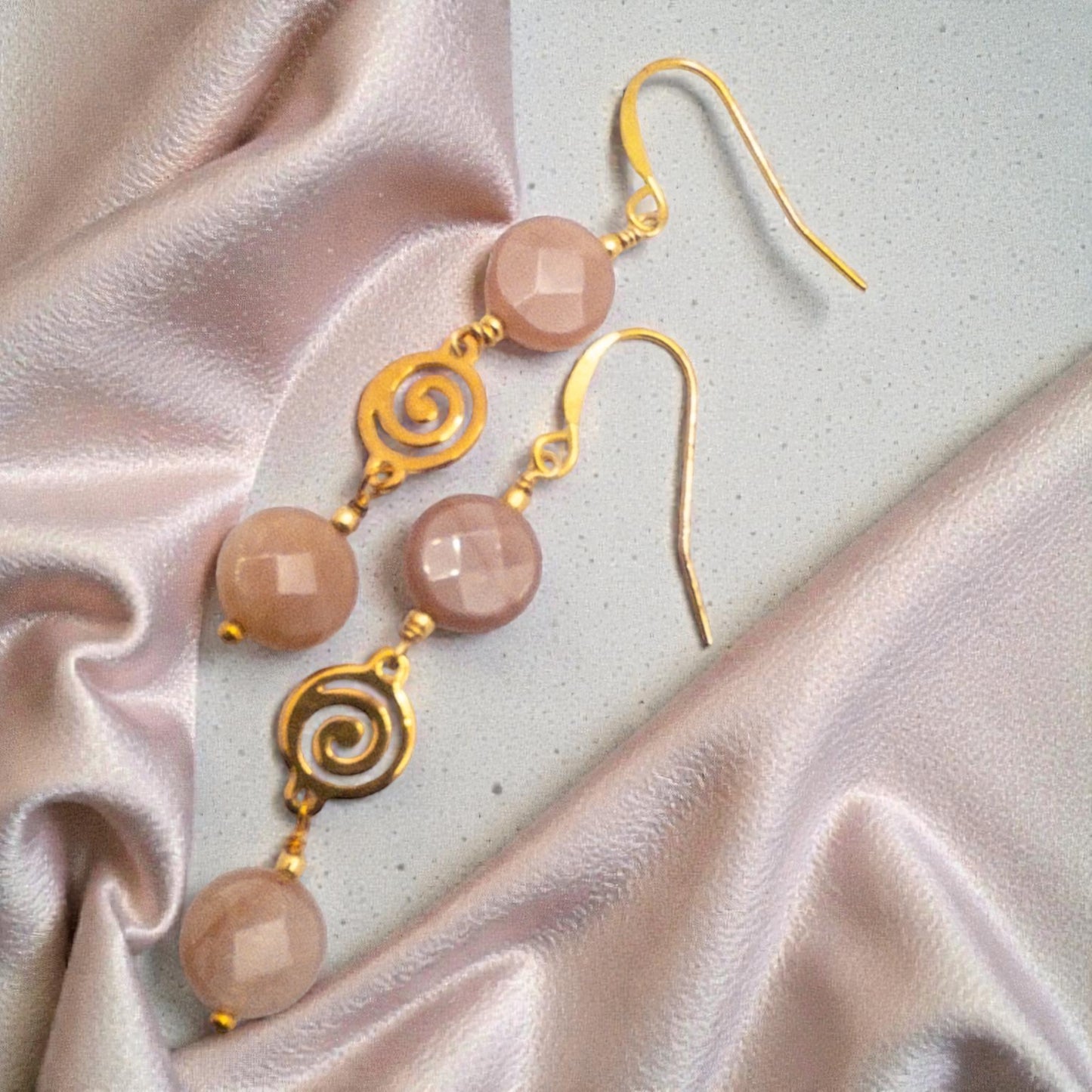Gold earrings with coin shaped peach moostone beads on a light fabric background