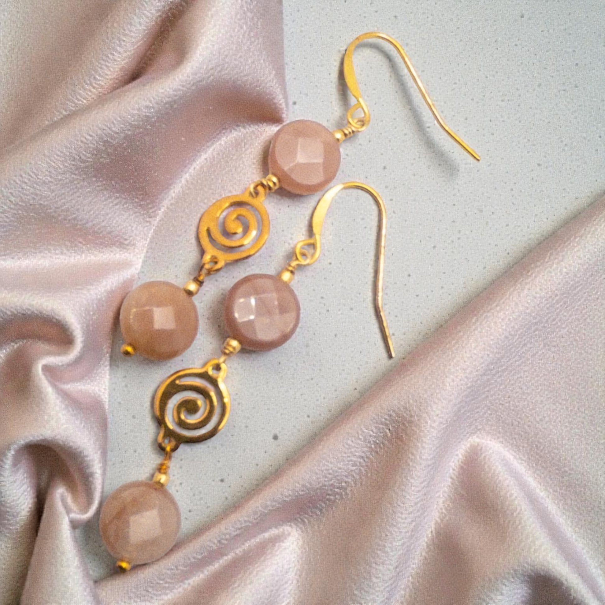 Gold earrings with coin shaped peach moostone beads on a light fabric background