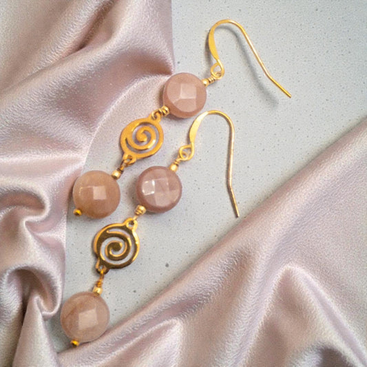 Gold earrings with coin shaped peach moostone beads on a light fabric background