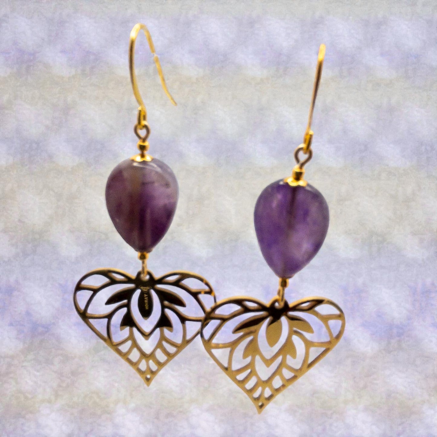 Pair of earrings with amethyst beads and gold heart-shaped filigree on a light background