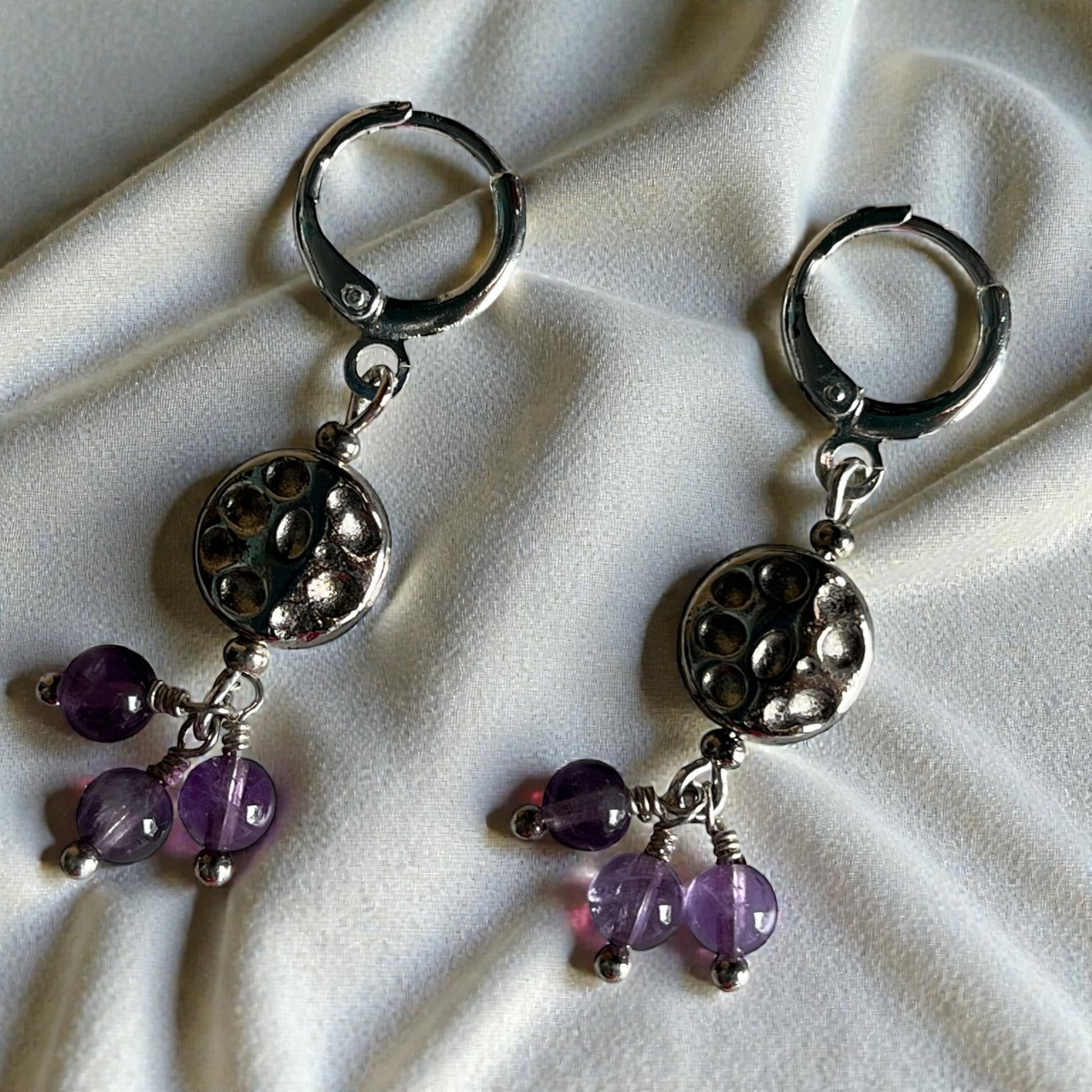 Silver earrings with purple beads on a white fabric background