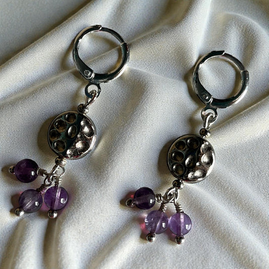 Silver earrings with purple beads on a white fabric background