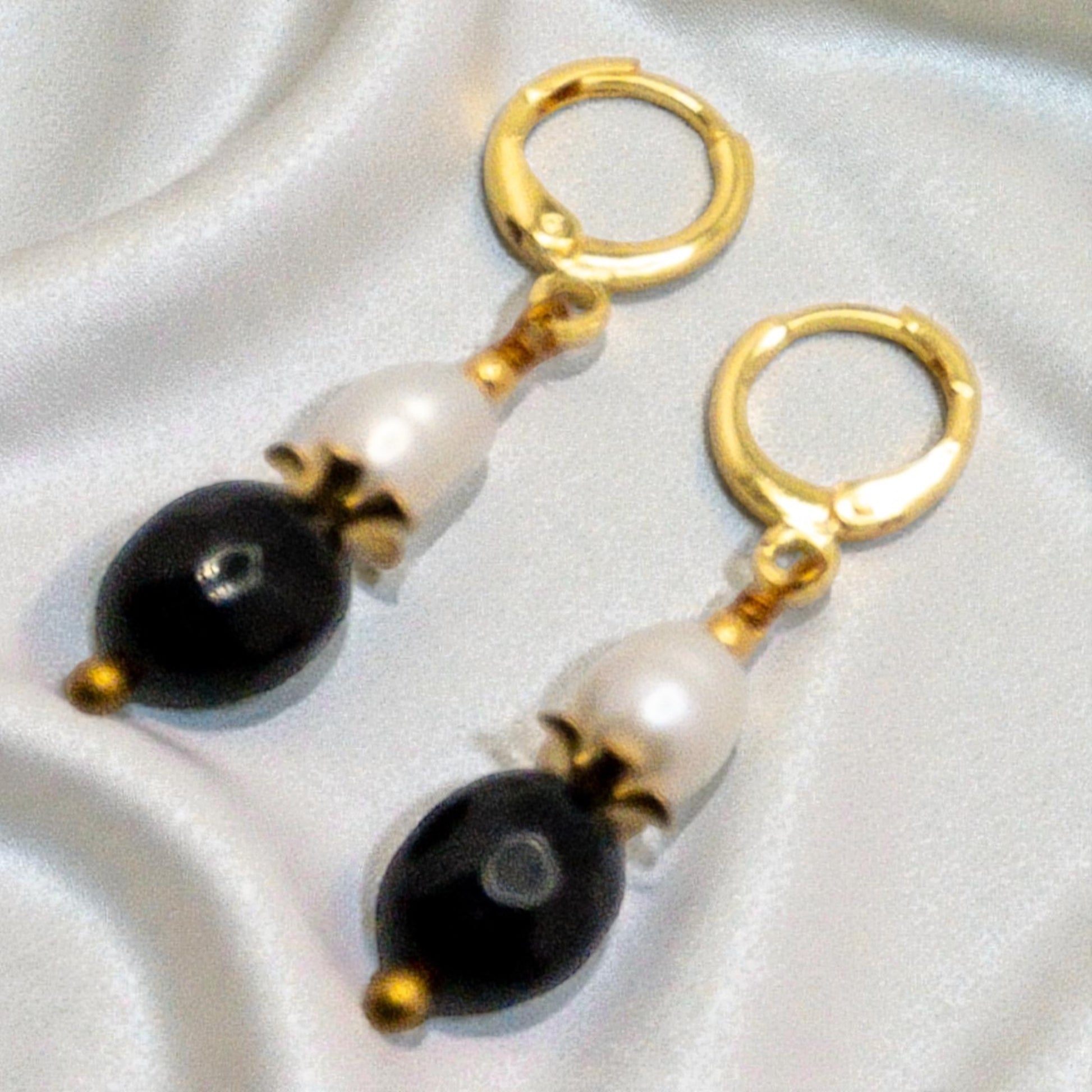 Pair of earrings with freshwater pearl and faceted black onyx bead  on a light gray background
