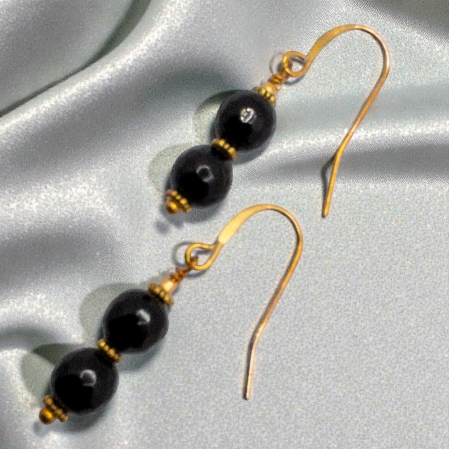 Pair of black onyx faceted beads separated by gold daisy spacers and suspended from gold french wire ear wirese