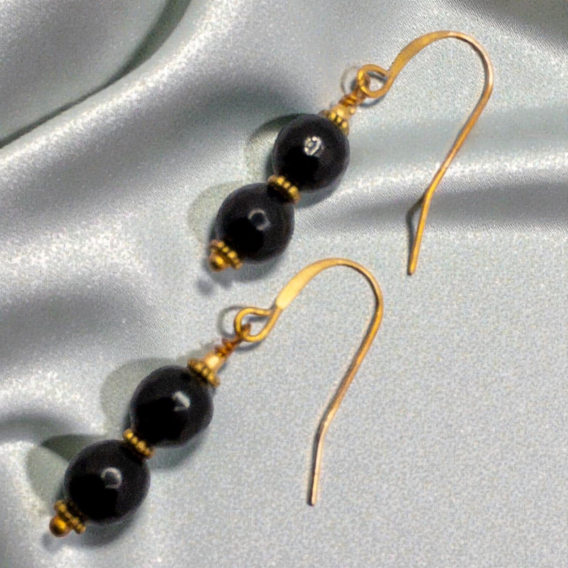 Pair of black onyx faceted beads separated by gold daisy spacers and suspended from gold french wire ear wirese