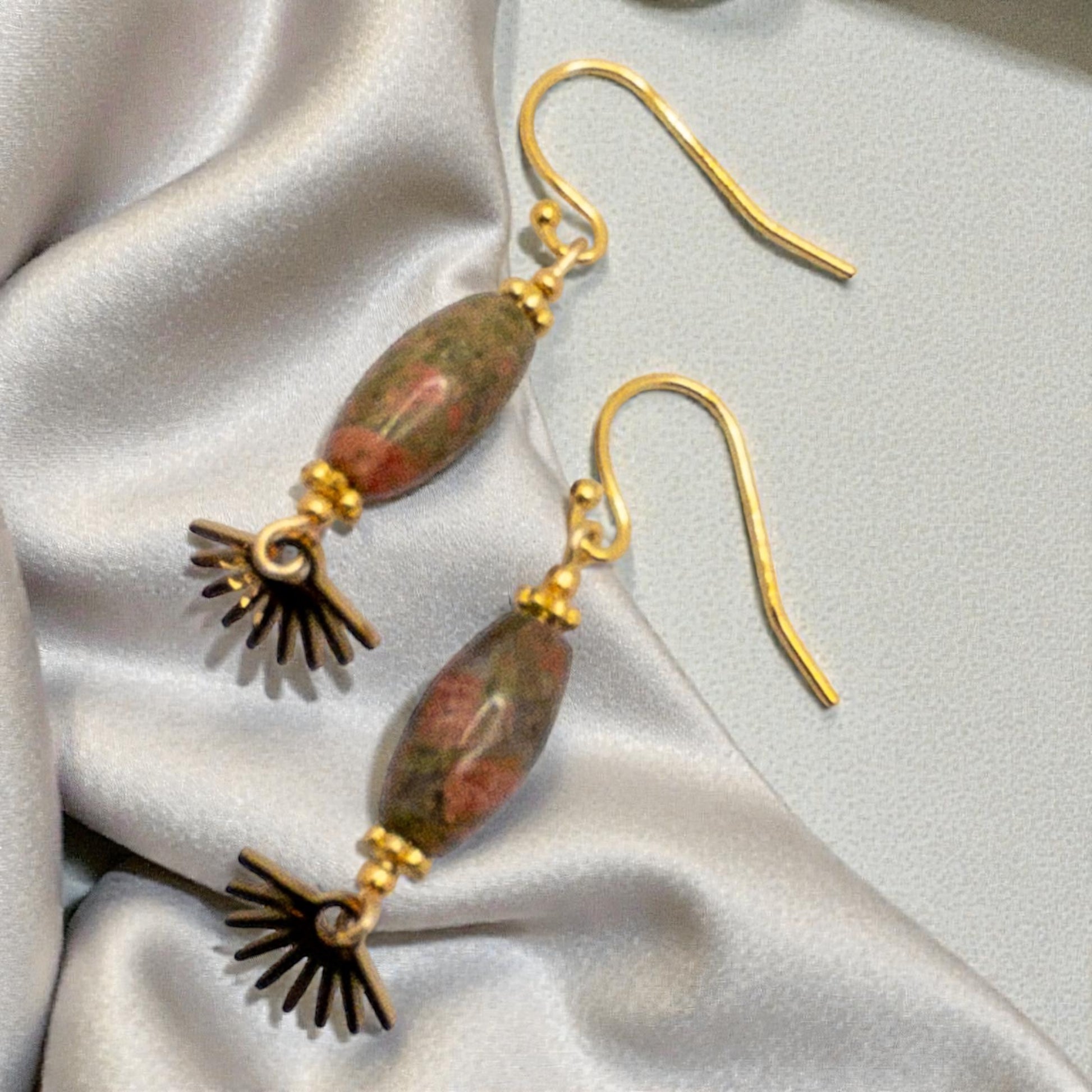 Pair of earrings with gold plated french hook ear wires, Unikite ( green and coral beads), and a starburst dangle  accents on a satin surface.