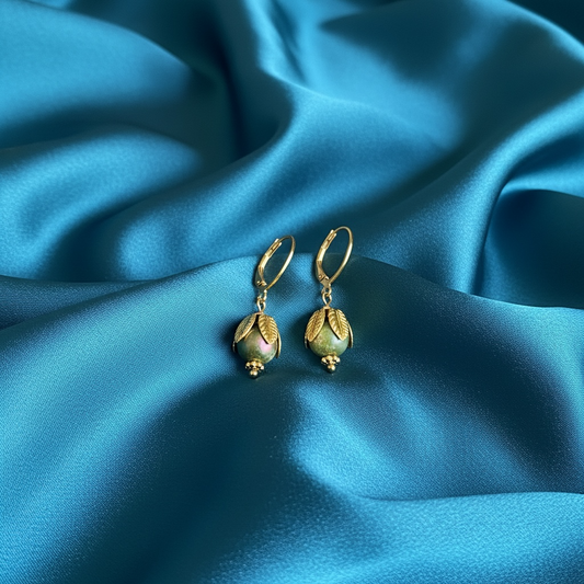 Gold earrings with green gemstones on a blue satin background