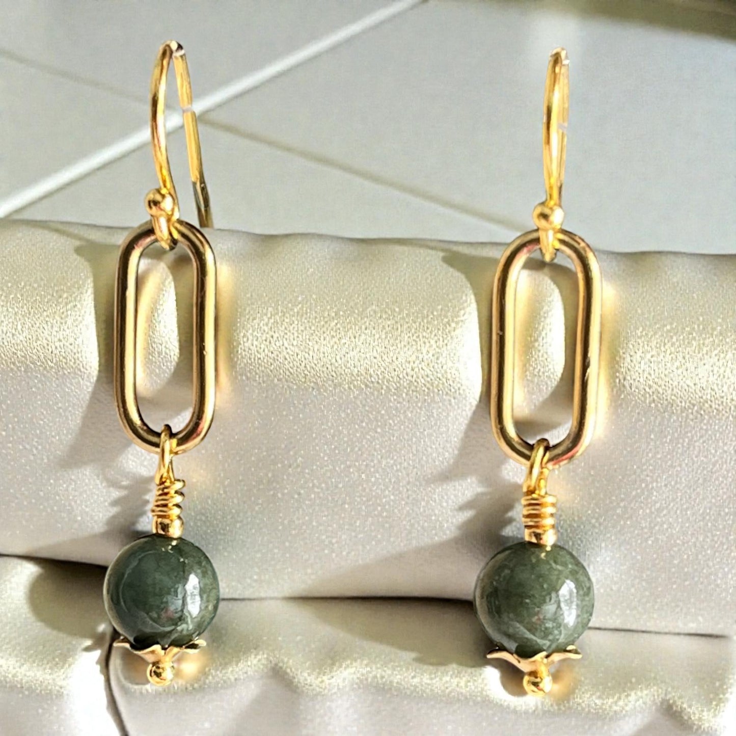 Gold earrings with green beads on a white surface