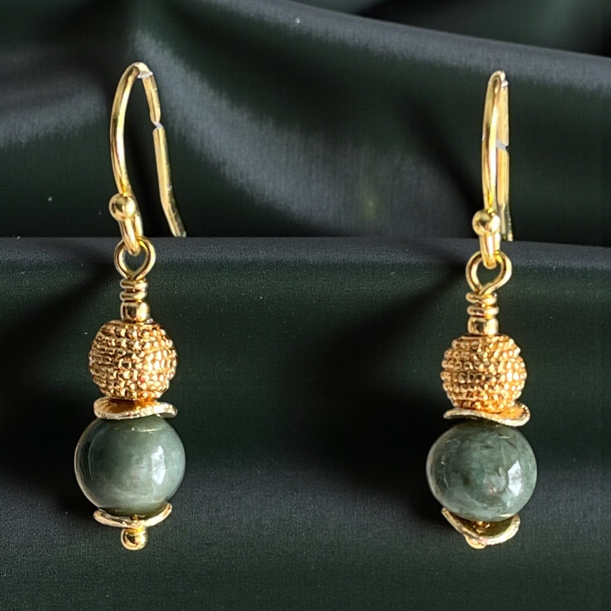 Gold and green bead earrings on a dark fabric background