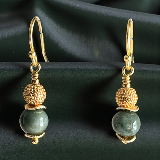 Gold and green bead earrings on a dark fabric background