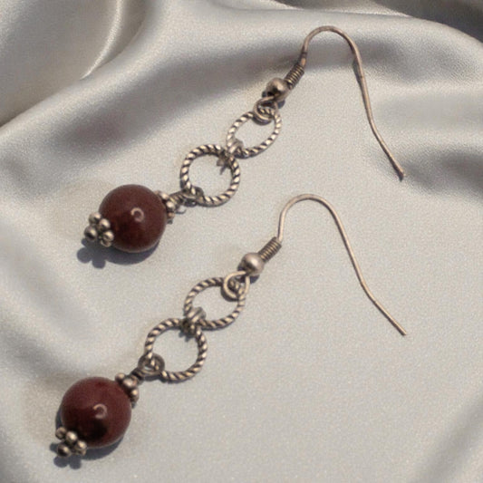 Pair of earrings with brick red bead  and silver loops on a light fabric background