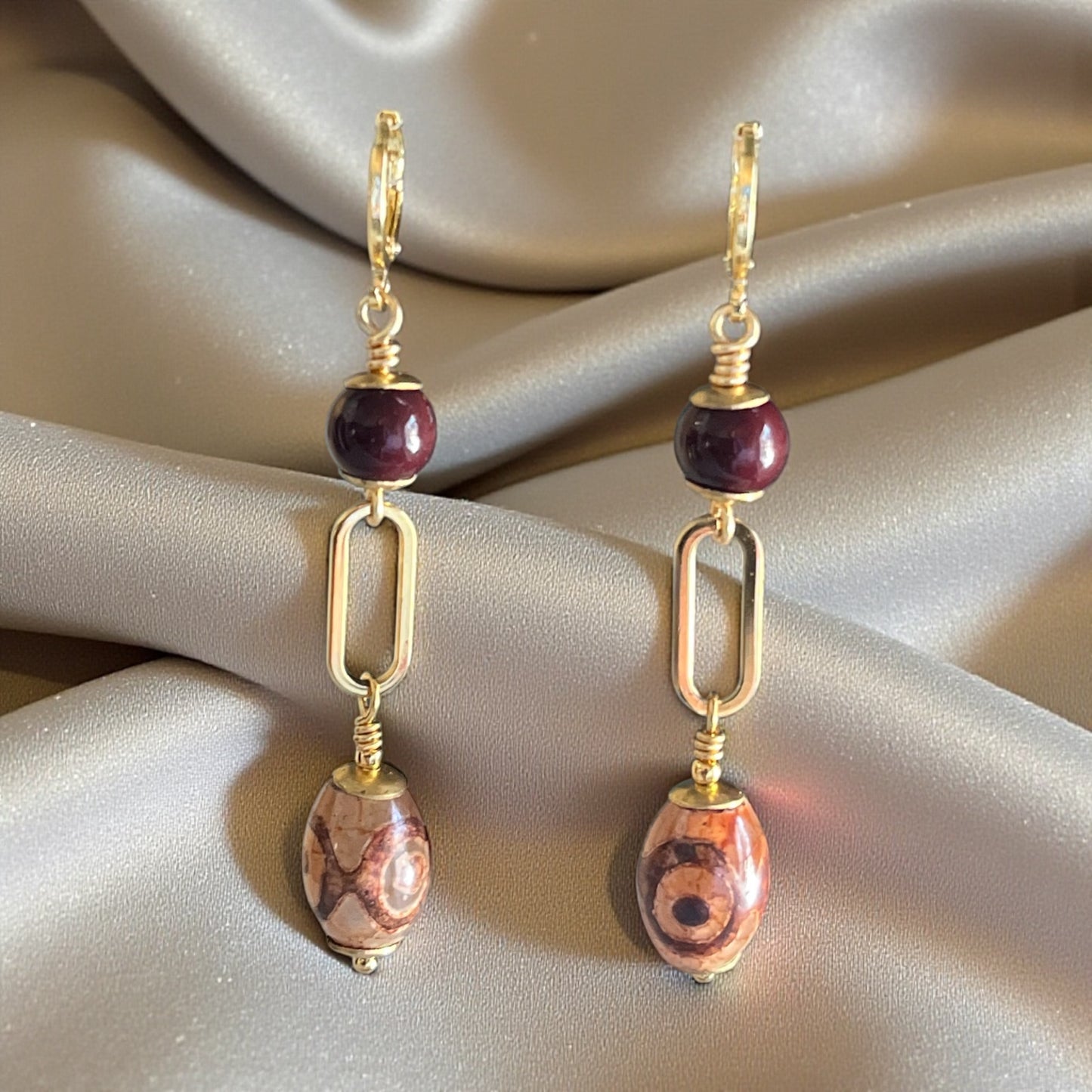 Gold earrings with brick red and brown beads on a beige fabric background