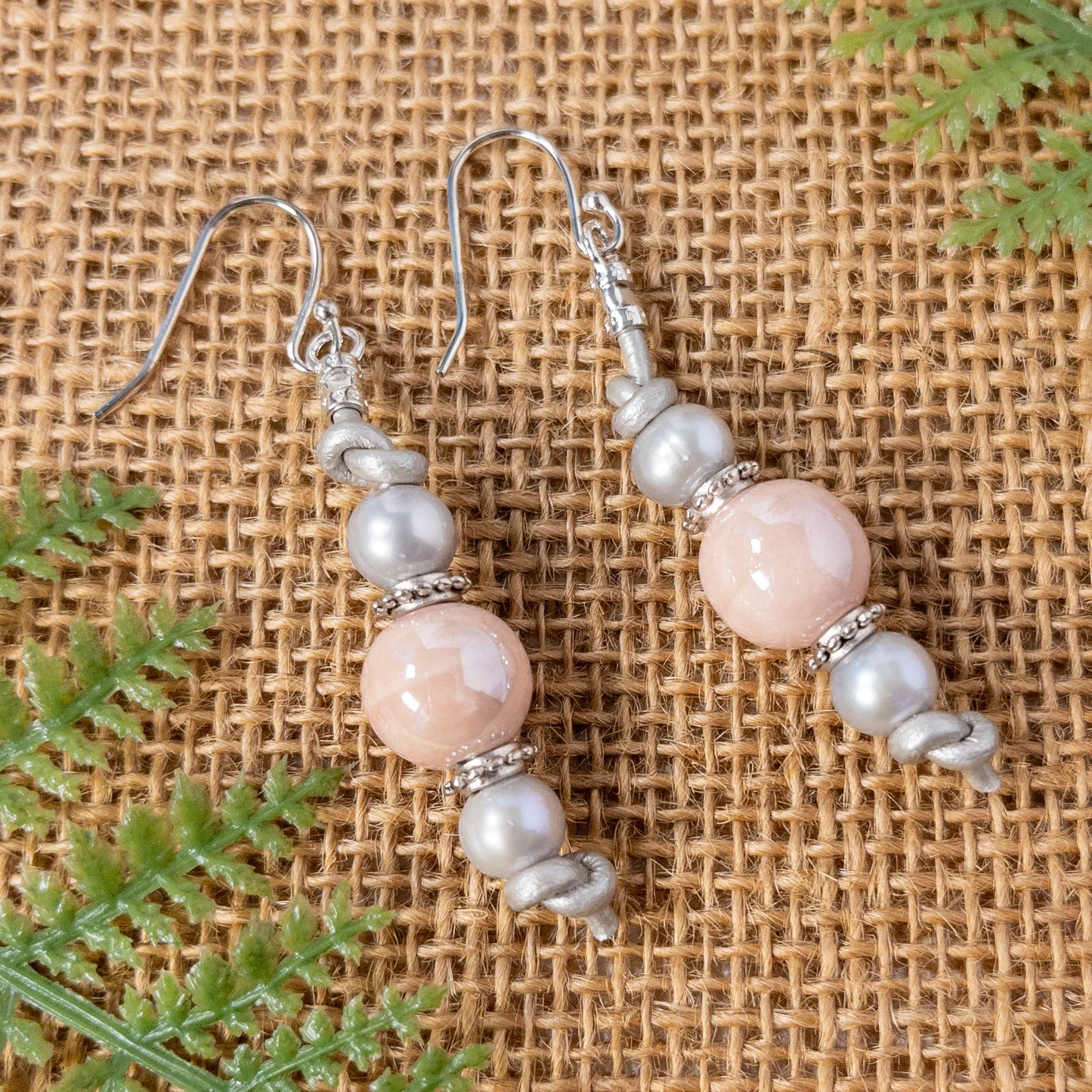 These earrings are approximately 2 inches in length and are made with petal pink ceramic round beads and silver fresh water pearls that are strung on grey leather cording.
