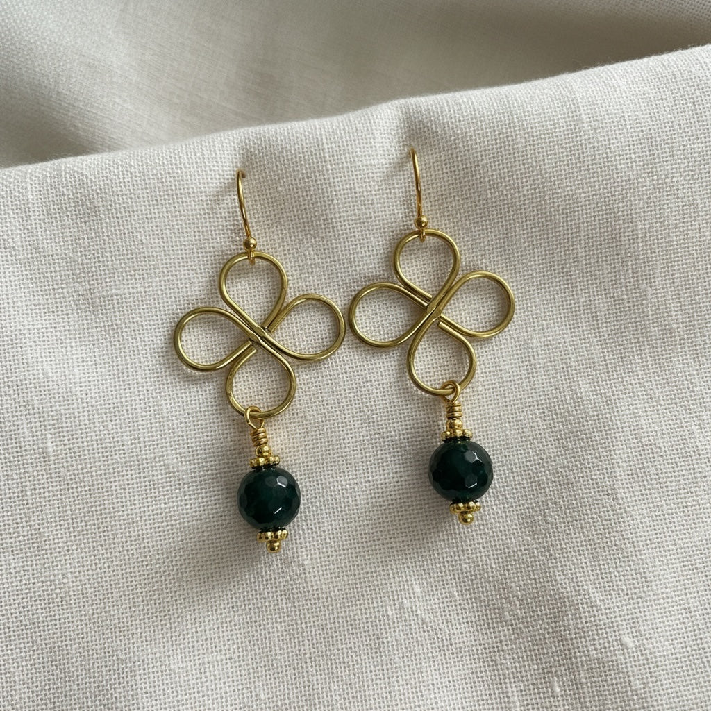 Blakeley Lane Jewelry gold wire clover drop earrings with faceted deep green beads on a white linen background.